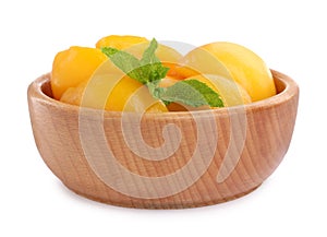 Halves of canned peaches with mint leaves in wooden bowl isolated on white