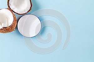 Halves of chopped coconut on blue background with cream jar