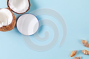 Halves of chopped coconut on blue background with seashells and cream jar