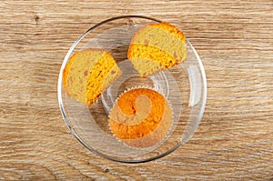 Halves of orange muffin, whole muffin in transparent saucer on table. Top view