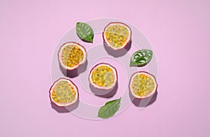 Halves of passion fruits maracuyas and green leaves on pink background, flat lay
