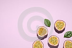 Halves of passion fruits maracuyas and green leaves on pink background, flat lay. Space for text