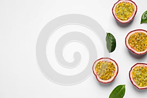 Halves of passion fruits maracuyas and green leaves on white background, flat lay. Space for text