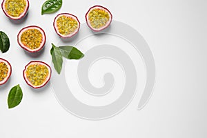 Halves of passion fruits maracuyas and green leaves on white background, flat lay. Space for text