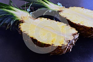 Halves of pineapple on black concrete background.