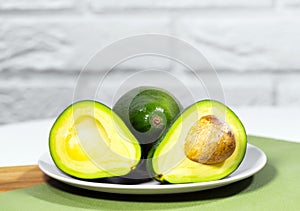 Halves of Ripe Avocado on bowl served on table, Green and white background, Healthy oily food, Keto diet