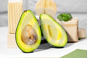 Halves of Ripe Avocado and micro green on wooden podium and stands served on table, white background, Healthy oily food