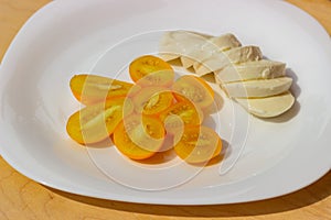 Halves of yellow tomatoes and sliced â€‹â€‹mozzarella on a white plate