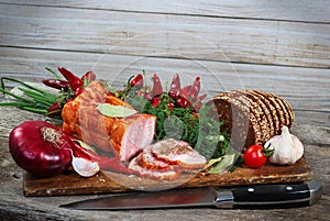 Ham and bread sliced with knife. Green and red vegetables on chopping board