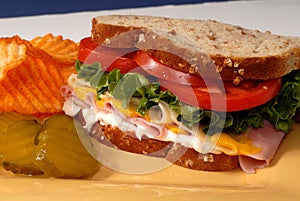 Ham, cheese, lettuce and tomato sandwich with pickles and chips