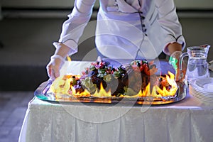 Ham cooking on grill with flames. Dish served with fire chef on background