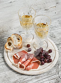 Ham, grapes, ciabatta bread and two glasses with white wine