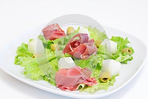 Ham with a melon and olives on a white plate.