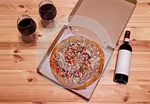 Ham pizza in box on wooden  table. Red wine near. Top view