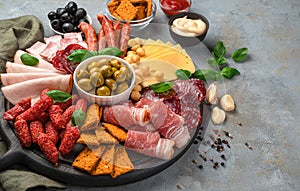 Ham, salami, bacon, cheese, olives and basil are sliced and stacked on a round chopping board.
