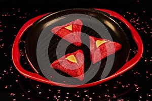 Hamans ears - hamantash are red, with Red Velvet flavor, on a black-red plate against a background with reflection