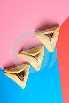 Hamantash filled-pocket cookie recognizable for triangular shape for Jewish holiday of Purim on red and blue background.