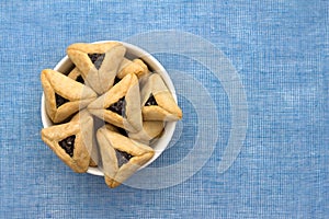 Hamantashen cookies or Aman ears, triangular cookies with poppy seeds on blue background