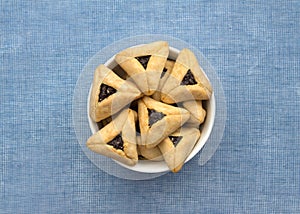 Hamantashen cookies or Aman ears, triangular cookies with poppy seeds on blue background