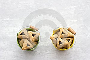 Hamantashen cookies or Aman ears, triangular cookies with poppy seeds in two colored buckets on gray background