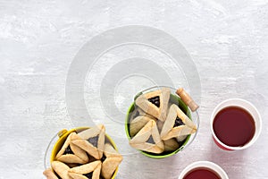 Hamantashen cookies or Aman ears, triangular cookies with poppy seeds in two colored buckets on gray background and hot tea in pap