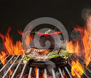 Hamburger with beef, lettuce, cheese and red pepper roasted on metal portable summer barbecue grill with flaming fire