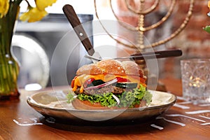 Hamburger with beef, mutton, vegetables, sauce and challah bun, on a plate, side view.