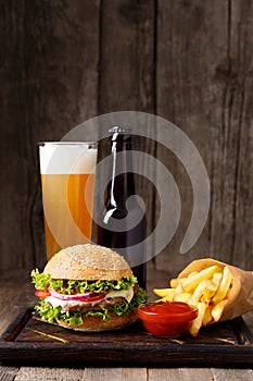 Hamburger, beer in a bottle and in a glass, french fries, sauce on a wooden background, fast food concept