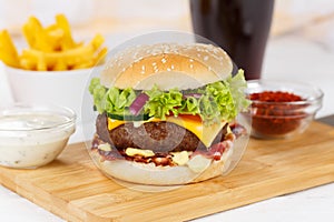Hamburger Cheeseburger meal fastfood fast food with cola drink and French Fries on a wooden board