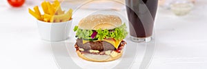 Hamburger Cheeseburger meal fastfood fast food with cola drink and French Fries on a wooden board panorama