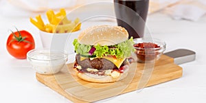 Hamburger Cheeseburger meal fastfood fast food with cola drink and French Fries on a wooden board panorama