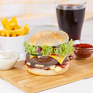 Hamburger Cheeseburger meal fastfood fast food with cola drink and French Fries on a wooden board square