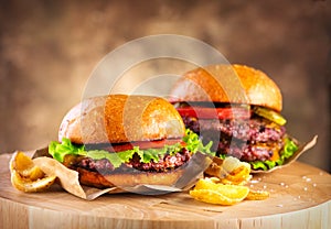 Hamburger and Double Cheeseburger with fries rotated on wooden table background. Cheeseburgers on fresh buns with succulent beef