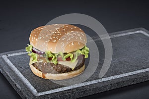 Hamburger with a double serving of meat, tomatoes, salad, onions on a wooden board in a restaurant.Copy space