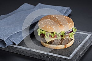 Hamburger with a double serving of meat, tomatoes, salad, onions on a wooden board in a restaurant.Copy space
