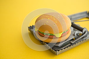 Hamburger fast food in a rat trap on yellow background copy space. Junk foods, unhealthy, people office lifestyle concept.