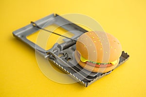 Hamburger fast food in a rat trap on yellow background copy space. Junk foods, unhealthy, people office lifestyle concept.