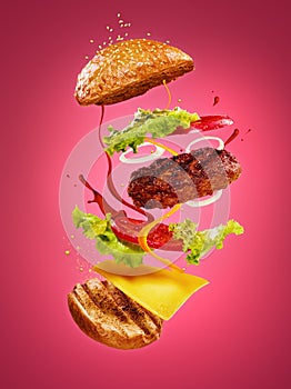 The hamburger with flying ingredients on rose background