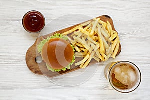 Hamburger, french fries, bbq sauce and glass of cold beer on a white wooden background, top view. Close-up
