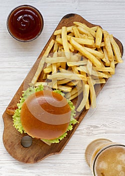 Hamburger, french fries, bbq sauce and glass of cold beer on a white wooden background, top view. Overhead, flat lay, from above