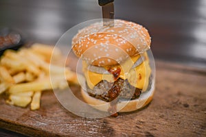 Hamburger, French fries and a Cup of sauce served on a wooden pl