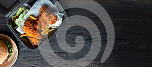 Hamburger, french fries and fried chicken in takeaway containers on the wooden background. Food delivery and fast food concept.