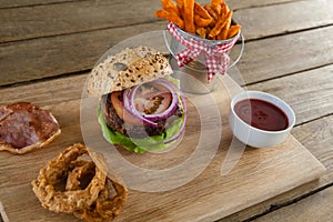 Hamburger, french fries, onion ring and tomato sauce on chopping board