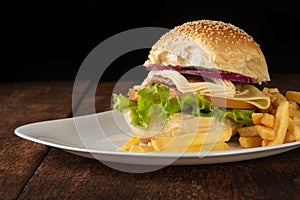 Hamburger and French fries placed on a white plate on rustic wood with black background, selective focus