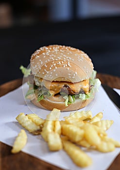 Hamburger with french fries served on a wooden plate.