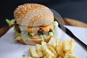 Hamburger with french fries served on a wooden plate.