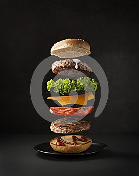 Hamburger ingredients flying on black background