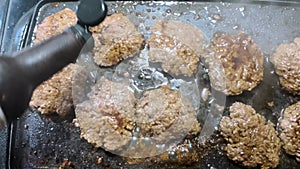 Hamburger patties frying on a griddle hand pouring seasoning on meat
