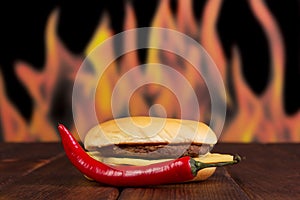 Hamburger and red hot pepper on background of flames.