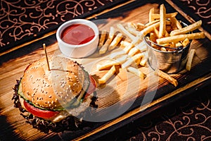 Hamburger with sauce and a bucket of french fries on a wooden plate